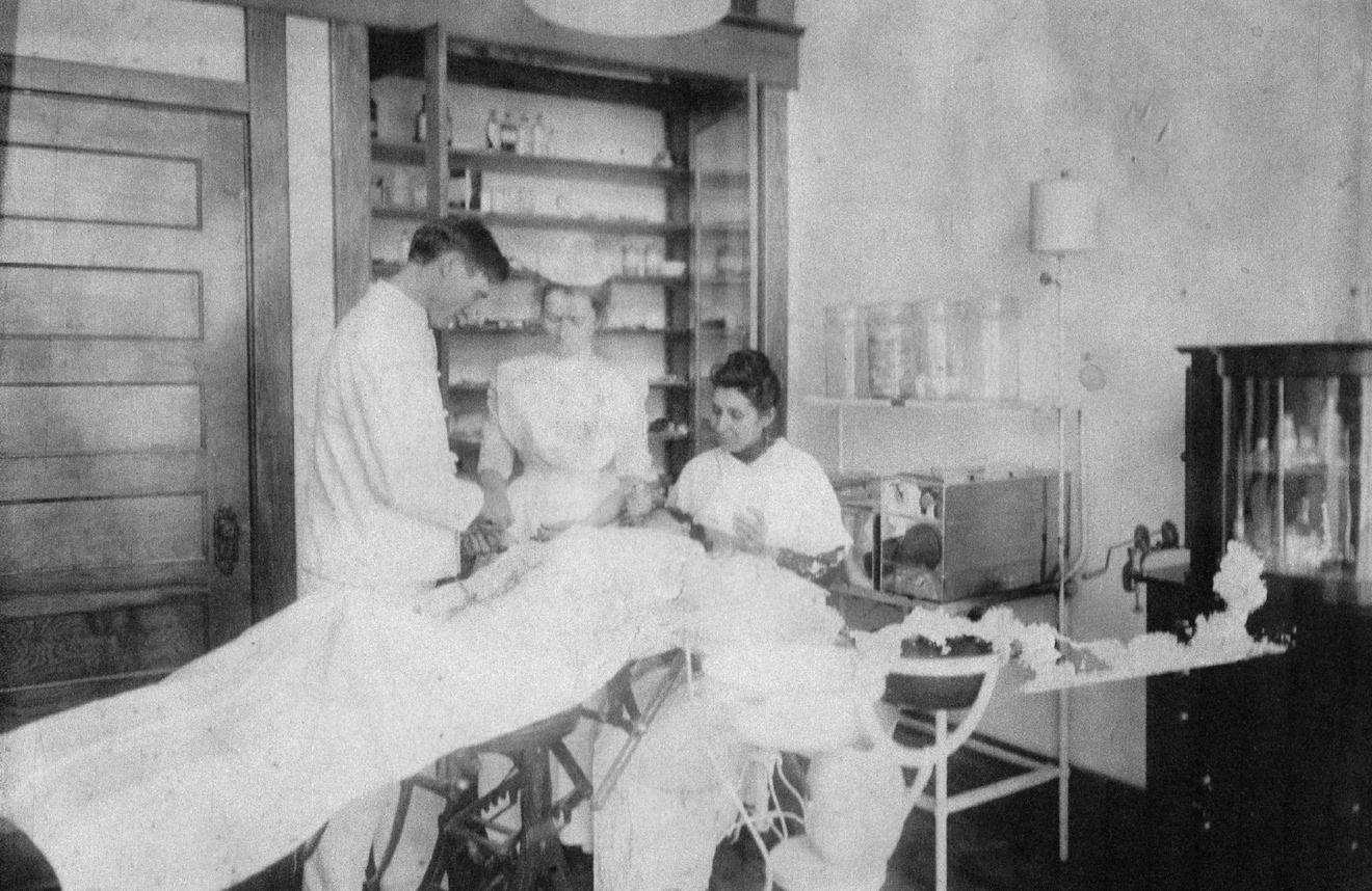 A black-and-white photo of three people gathered around a patient. More description below.