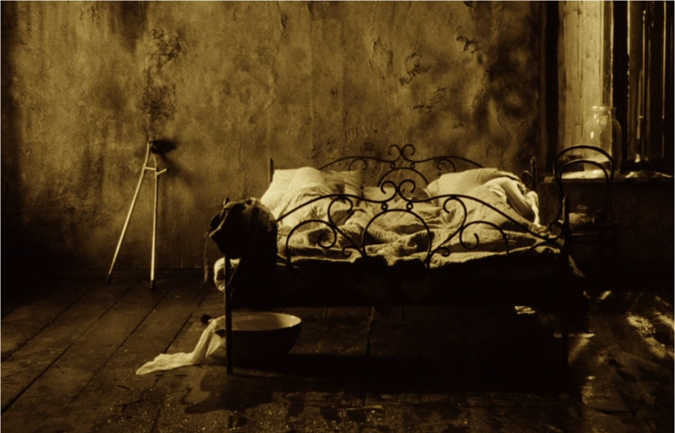 Photo of a bed with three figures sleeping in it, a basin underneath it, and crutches resting on the wall next to it