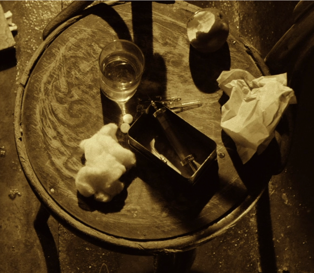 Photo of a round table with a glass of water, half-eaten apple, crumpled paper, cotton wool, medical syringe, and two pills resting on top