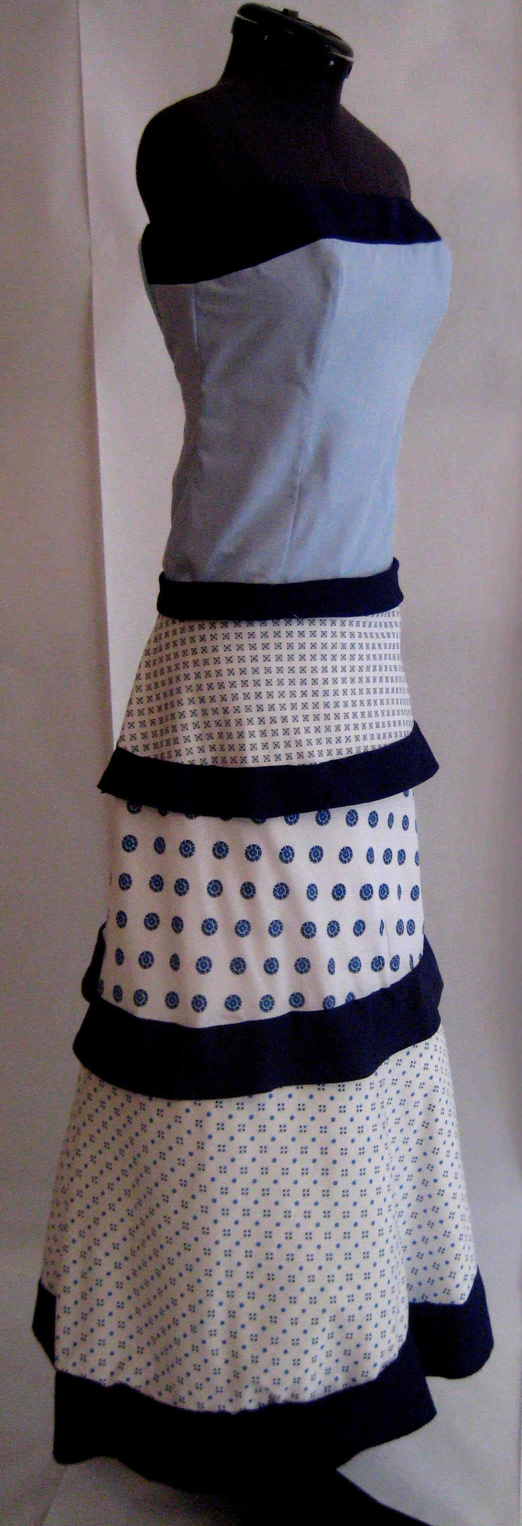 Image showing a side view of a dress on a dress form, with the bodice made of light blue fabric and the skirt made of 3 patterned fabrics separated by black strips