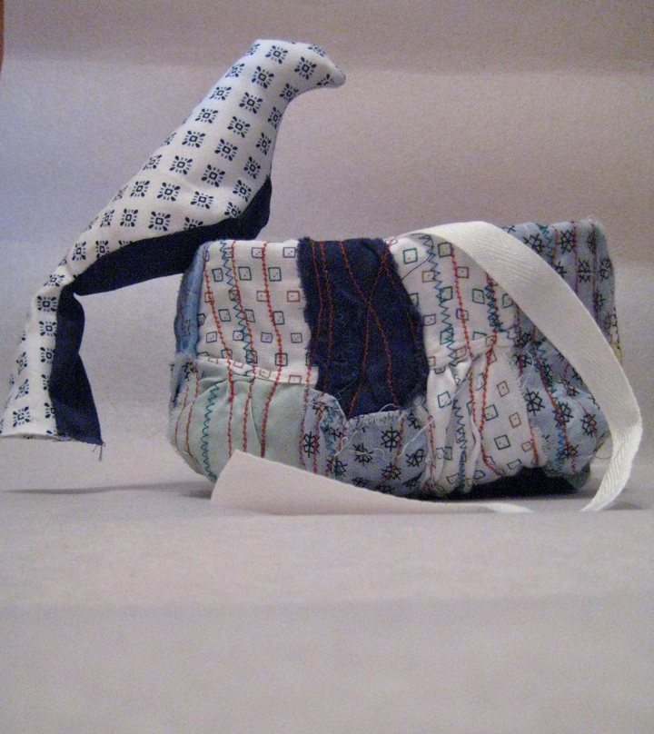 Image showing a sewn sculpture of a bird sitting on the edge of a nest, both composed of various pieces of hospital gown fabric