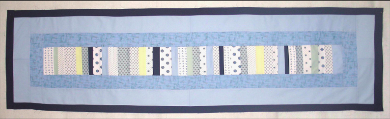Image showing a rectangular, quilted work consisting of strips of various hospital gown fabrics surrounded by borders of hospital gown fabric