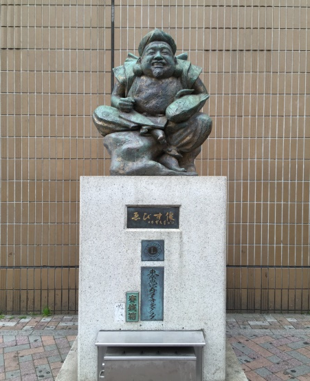 A photograph of statue representing the Ebisu figure. The figure is seated and has a large head and a short, rounded torso.
