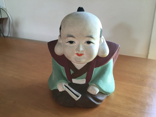 A photograph of a porcelain figure of Fukusuke. The figure is kneeling and has a large head with large earlobes.