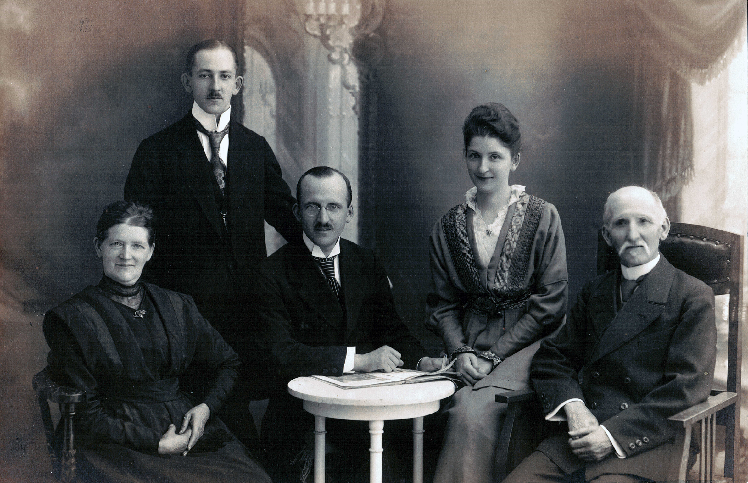 A black and white photograph with four people sitting and one standing. In the center of the photograph are Richard Listmann, Carl Listmann, and Emilie Rau. Their mother is to the left and to the right is their father.