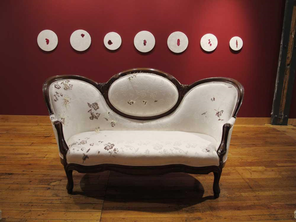 An ornate couch displayed in front of a red wall that has seven fabric circles hanging from it. More description below.