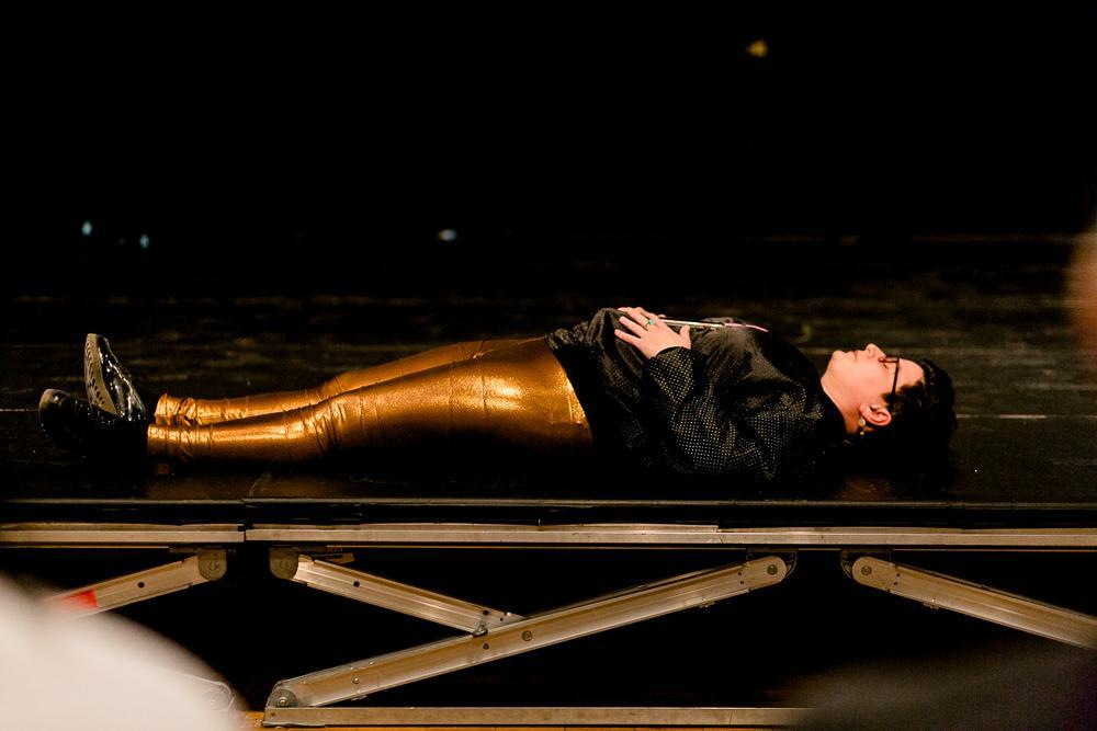A photograph of a woman with gold pants and black top lays on her back on a platform. More description below.