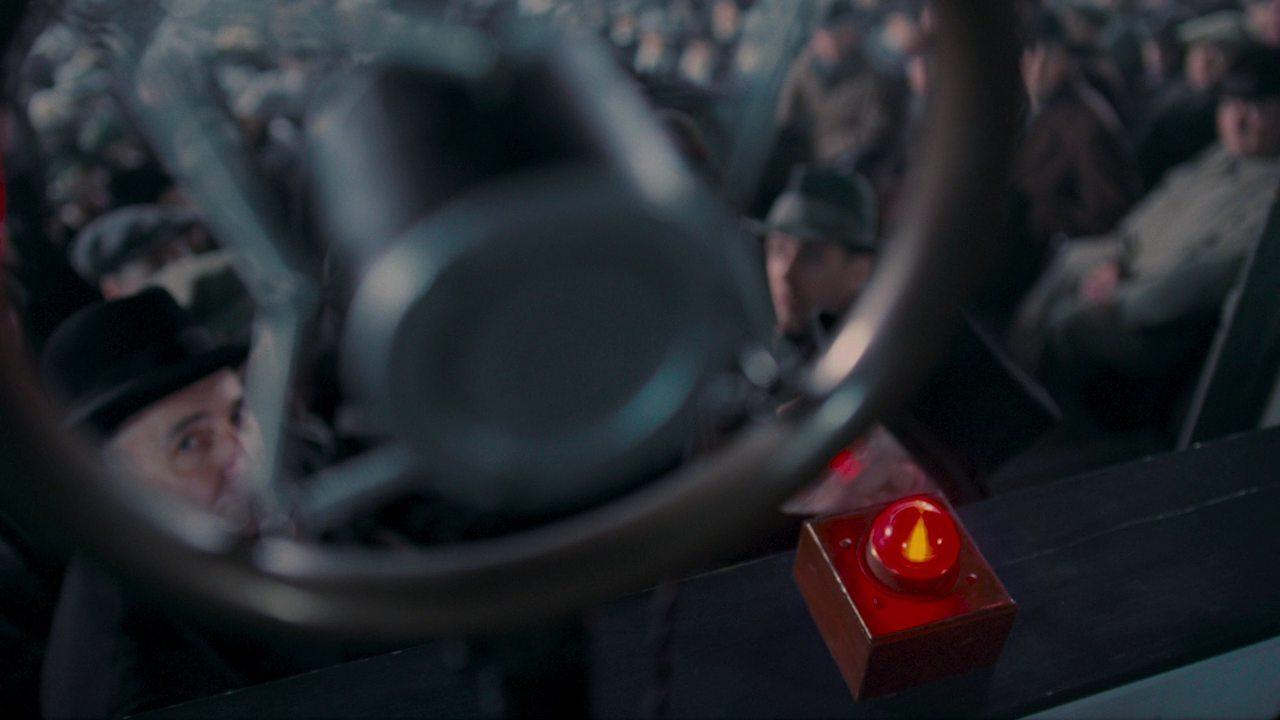 Close-up of a microphone and red light with a crowd of people visible in the background. More description below.